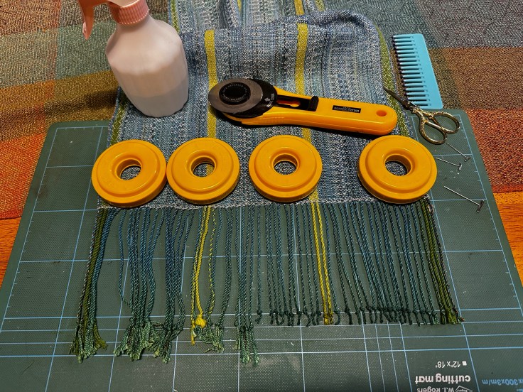 Weights on fabric, fringed ends on a scarf being trimmed