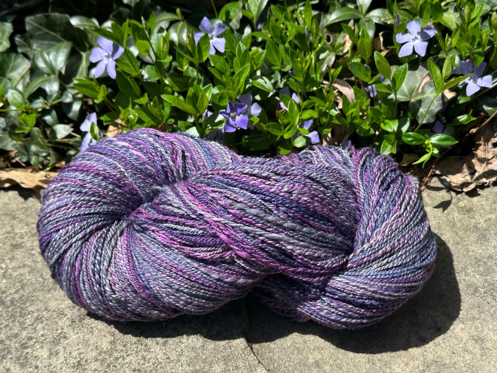 Skein of purple hands-on yarn on a rock in front of vinca plants